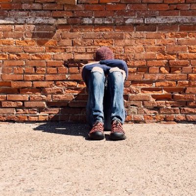 Person with head in their hands against red brickwall.